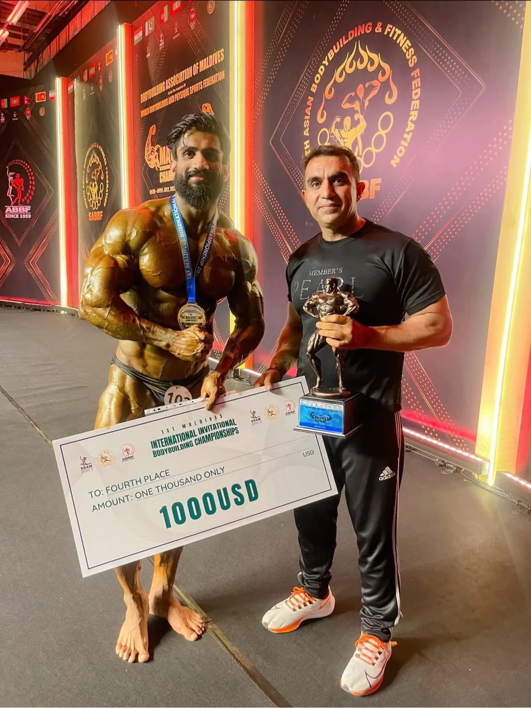 A Genetix athlete holding a US$1,000 prize cheque beside his coach